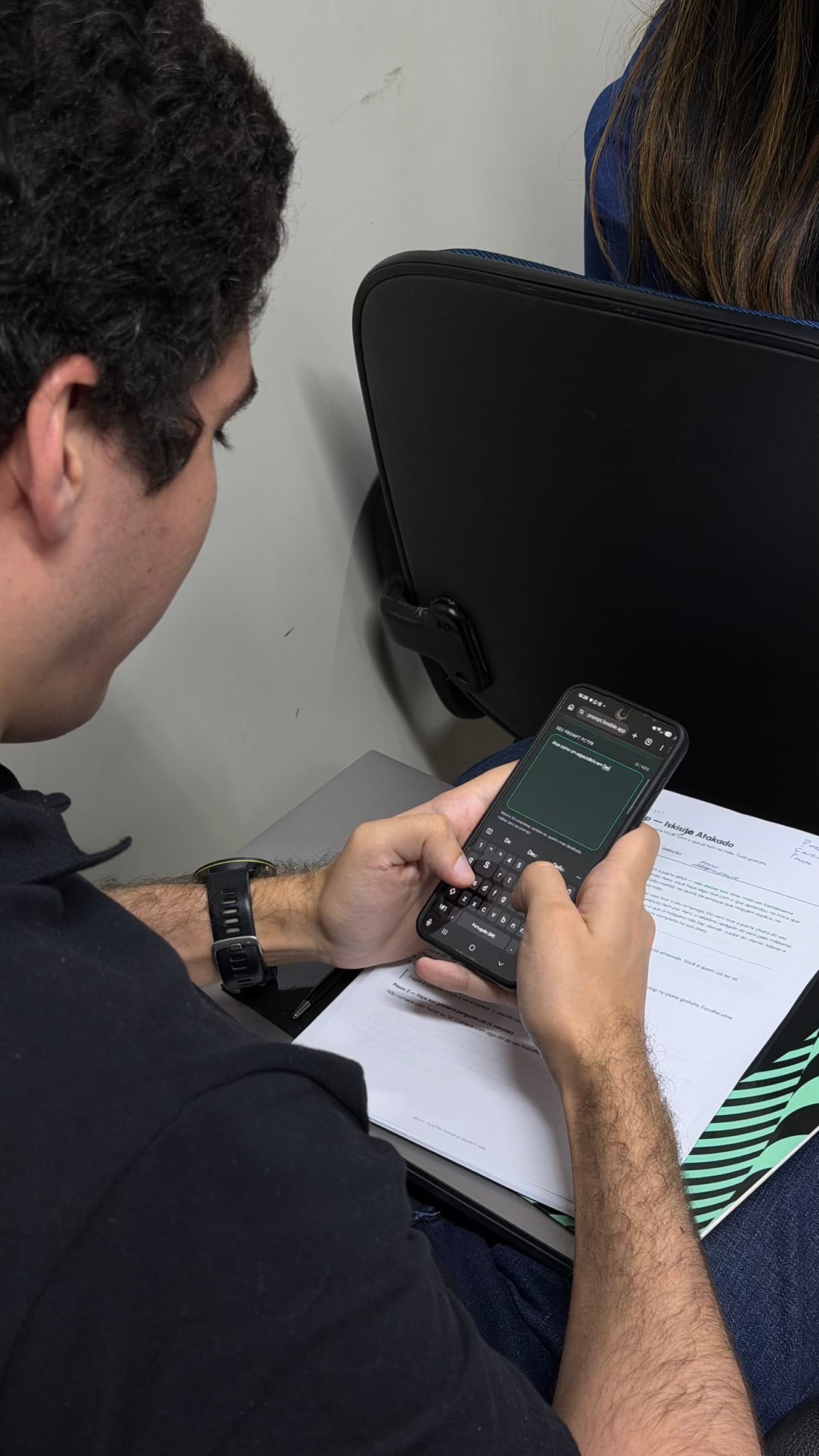 Participante escrevendo um comando no celular, apoiado no material impresso do workshop