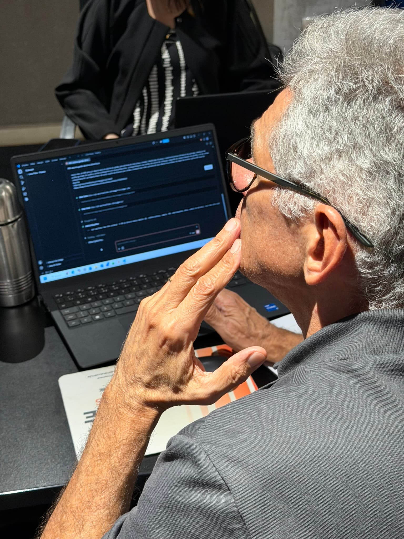 Aluno de cabelos grisalhos e óculos observa a tela do notebook com uma ferramenta de inteligência artificial aberta