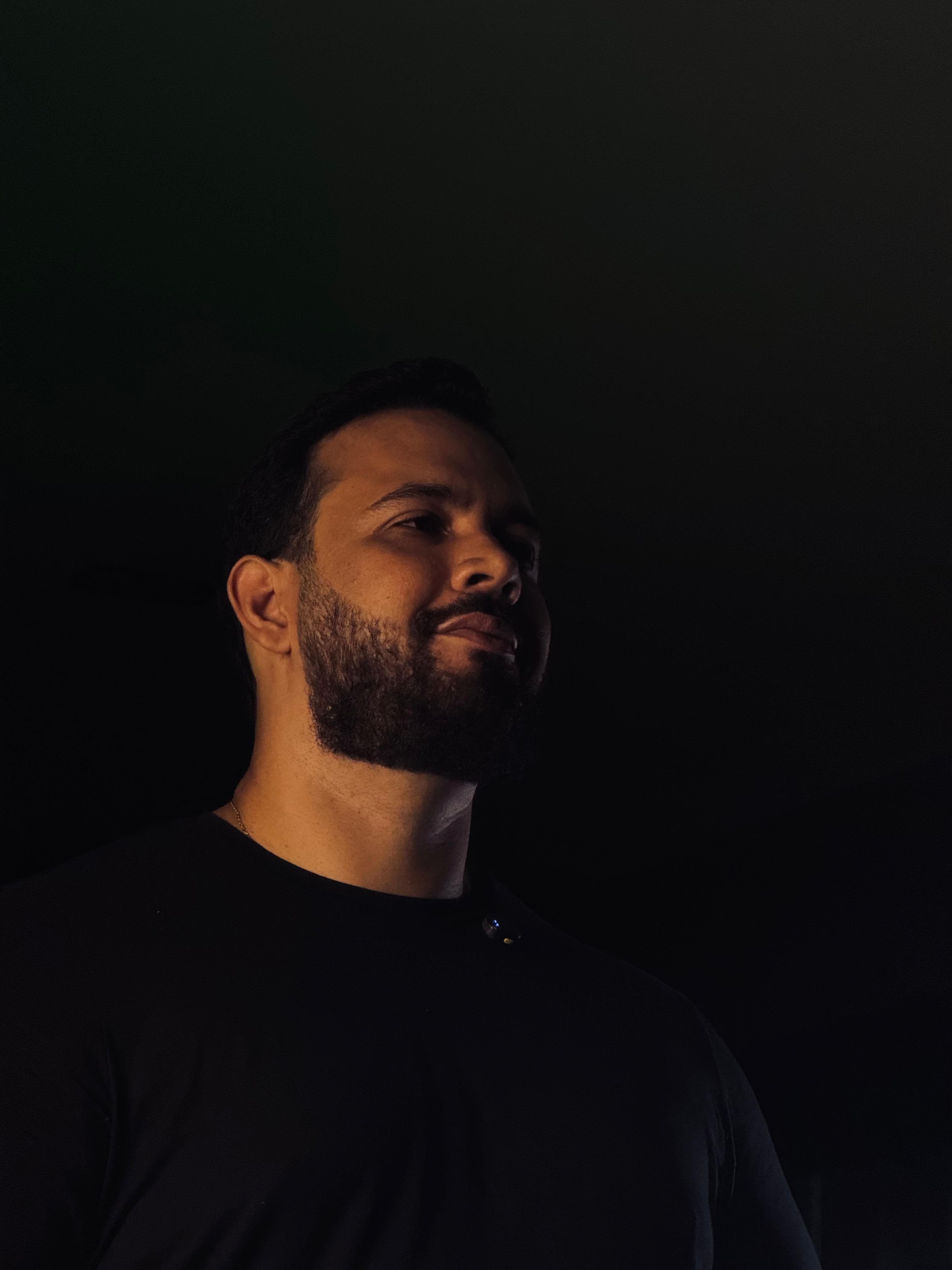 Retrato em meia-luz do mentor de camiseta escura, olhando para o alto contra o fundo preto
