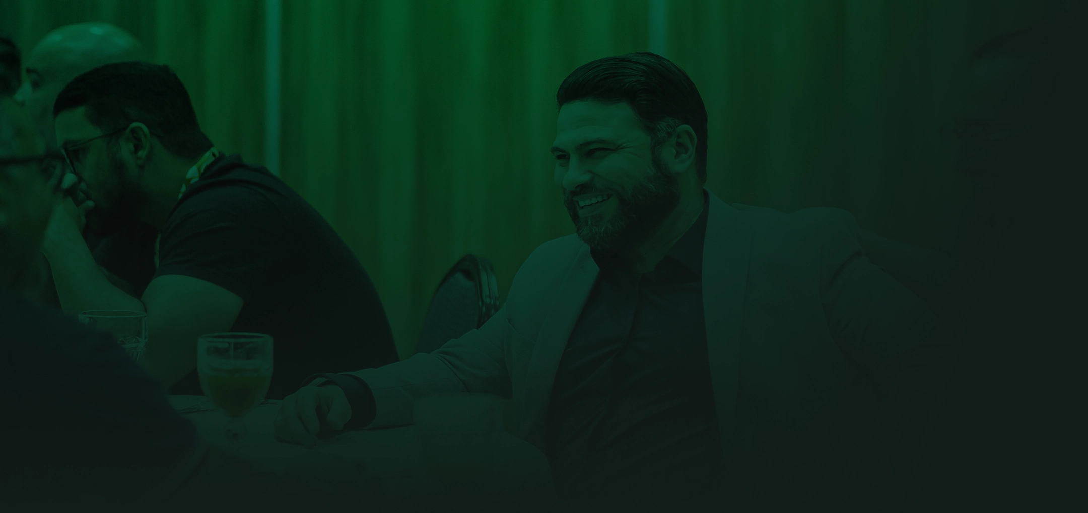 Homens de traje social conversando e rindo em torno de uma mesa de confraternização